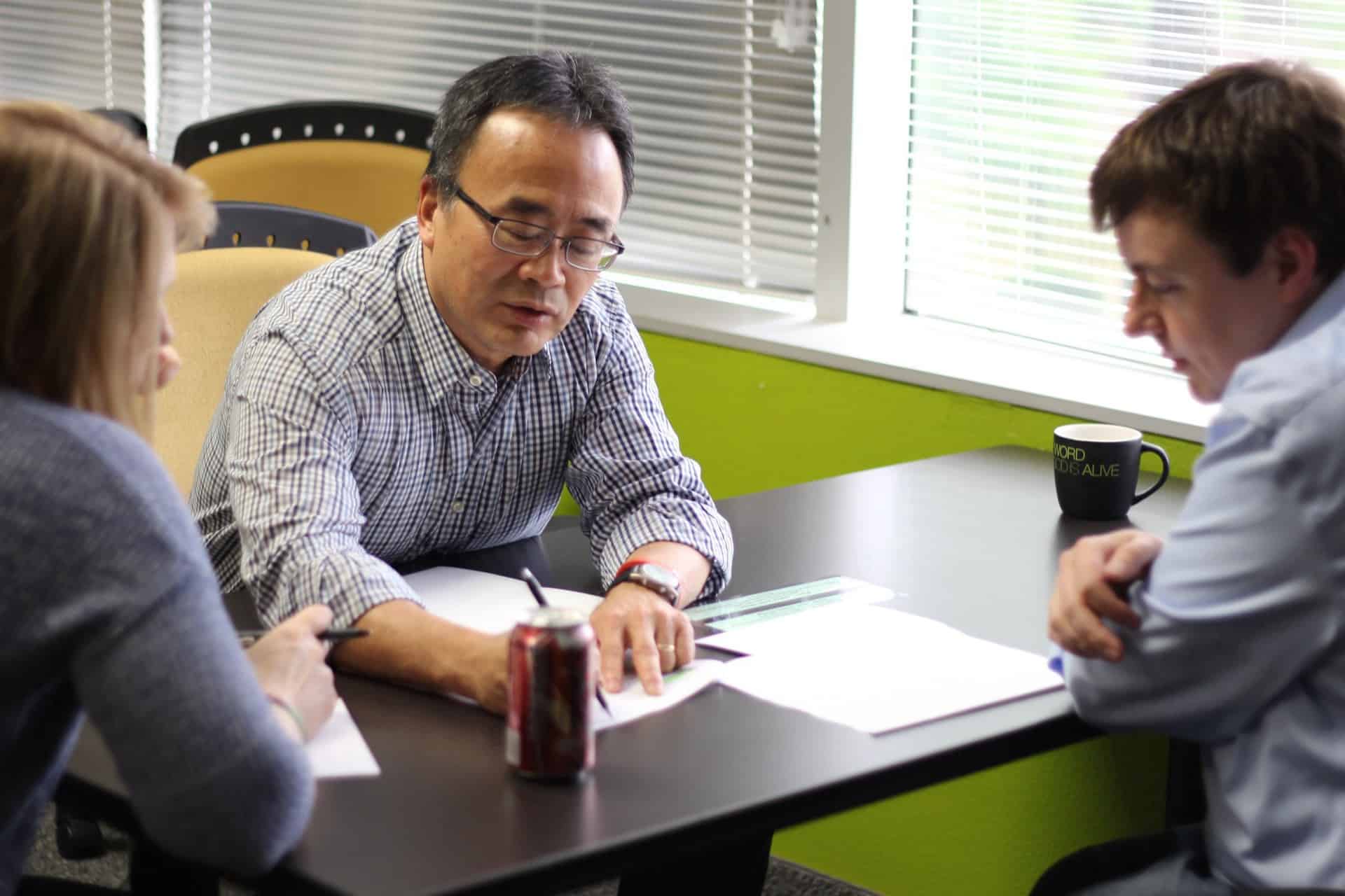 A man writing while conversing with two people during an HCD workshop