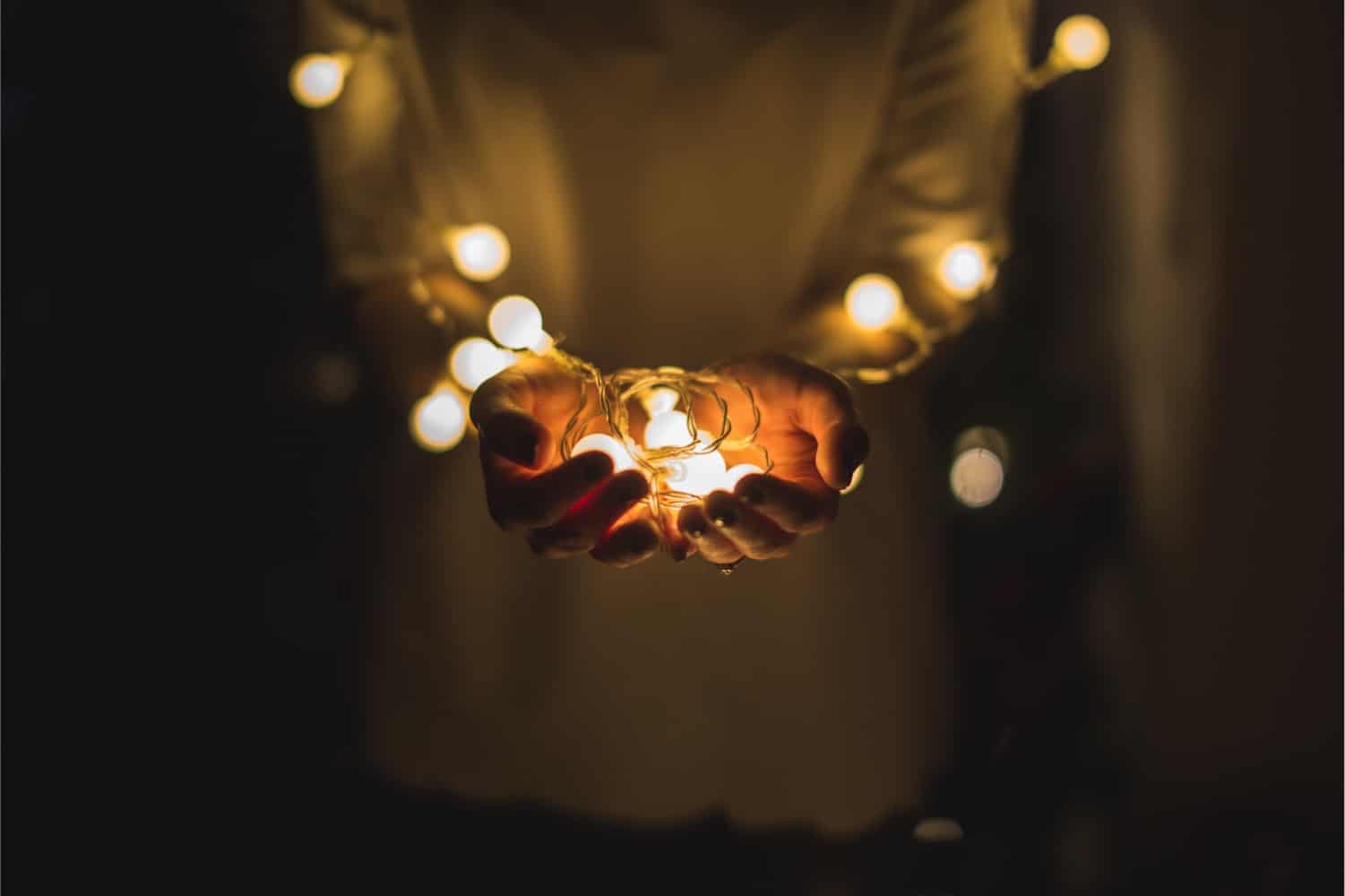 A person holds a bundle of glowing holiday lights in their hands