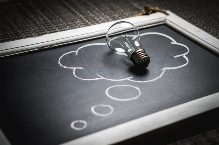 A small chalkboard with a thought bubble drawn on it and a lightbulb sitting on top of the bubble