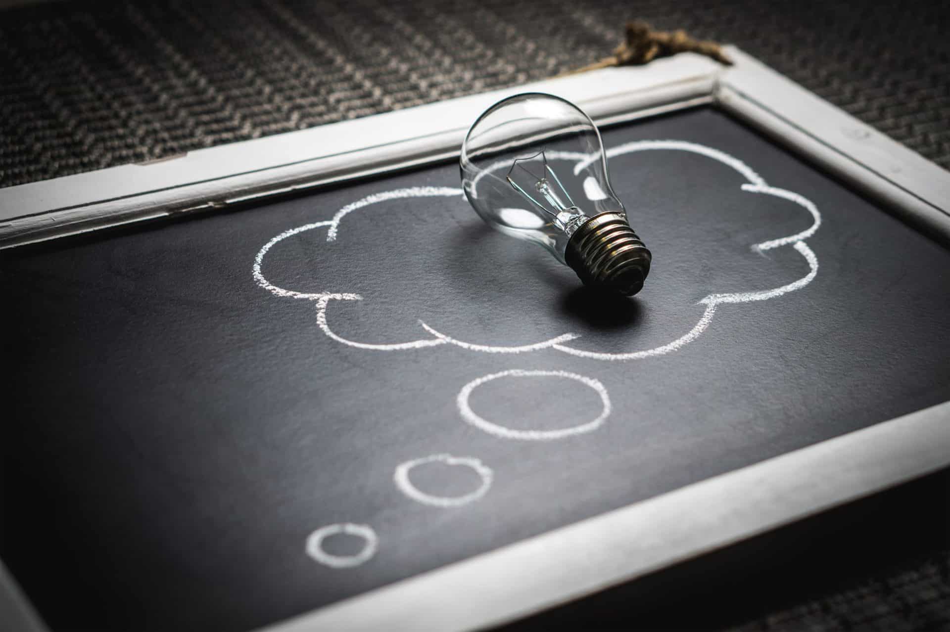 A small chalkboard with a thought bubble drawn on it and a lightbulb sitting on top of the bubble