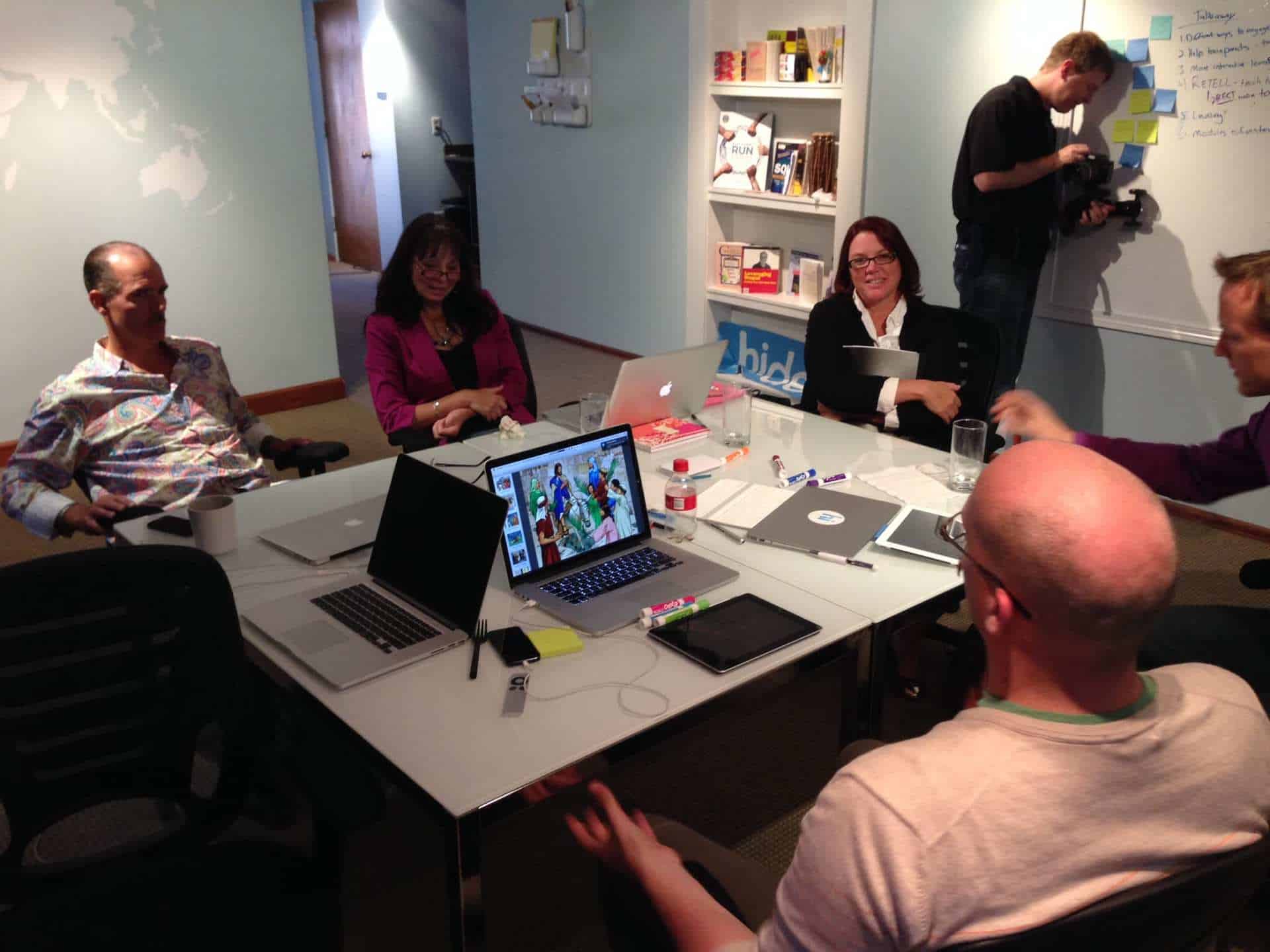 Several men and women collaborating at a table with many laptops on it.