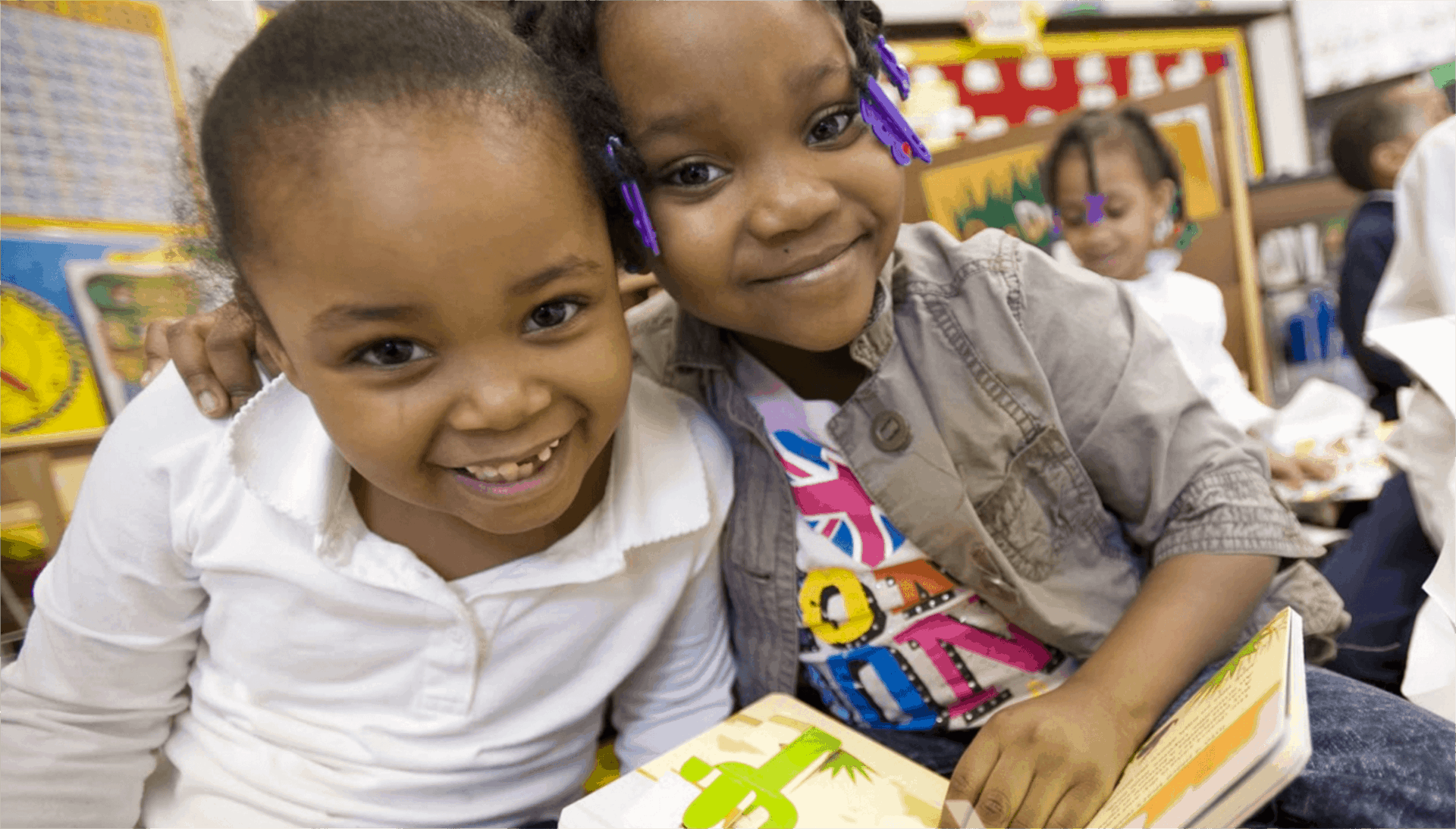 Two young girls reading a book and smiling for the camera