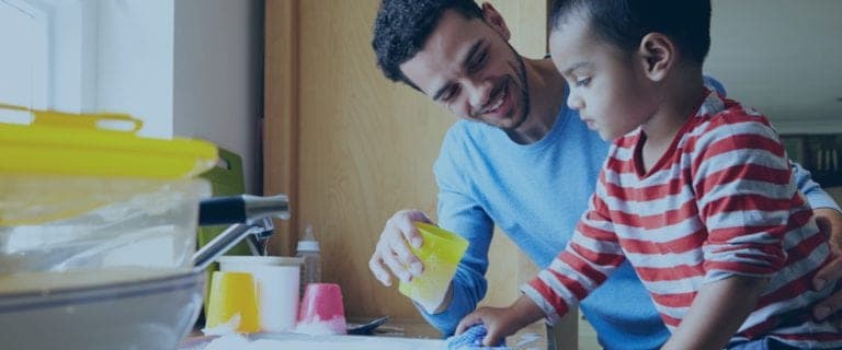 A father teach a young boy how to clean his cup in the sink.