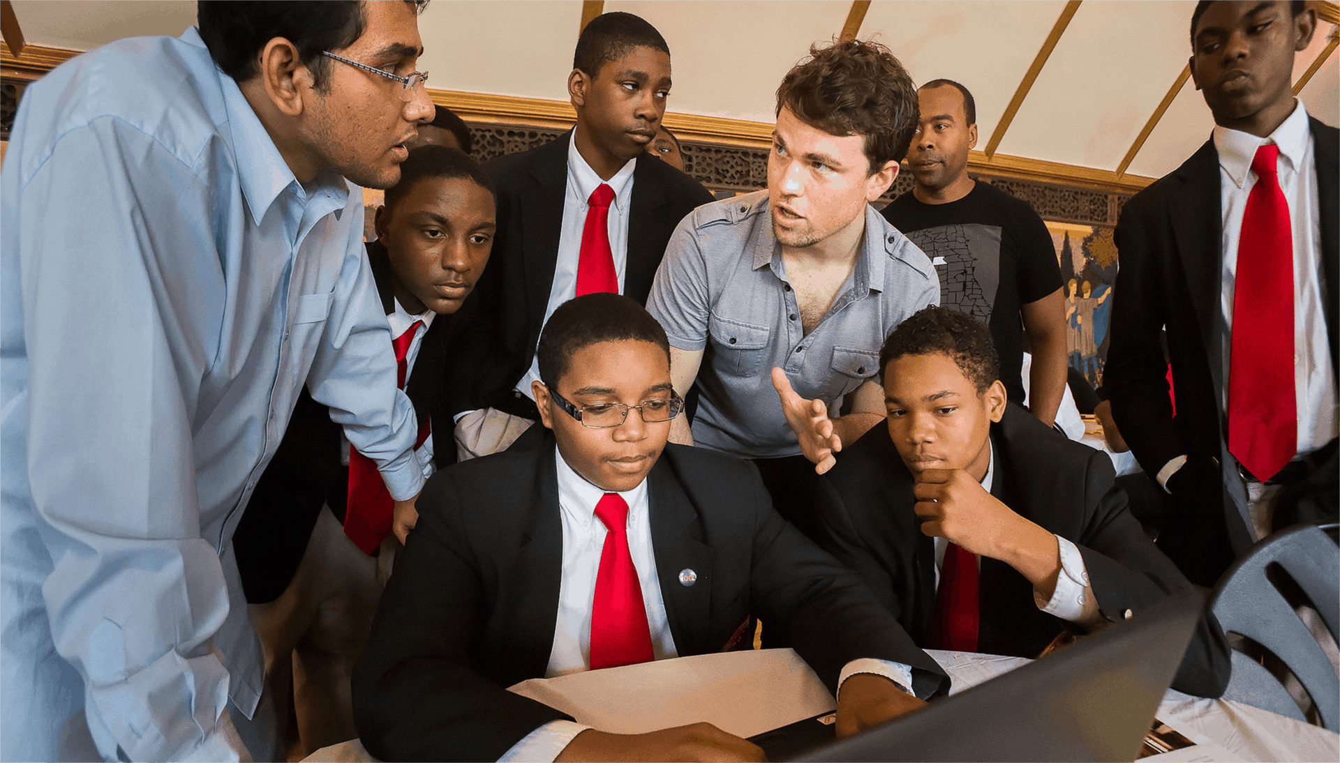 mt-1 A group of students and teachers sit gathered around a laptop during a design workshop