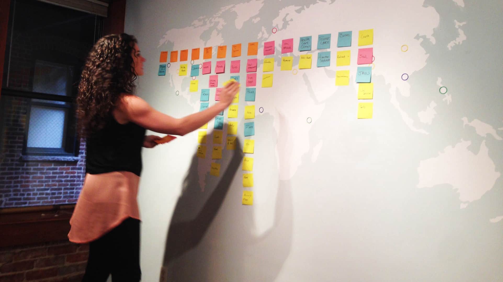 A woman places a sticky note on a wall during a CauseLabs strategic workshop