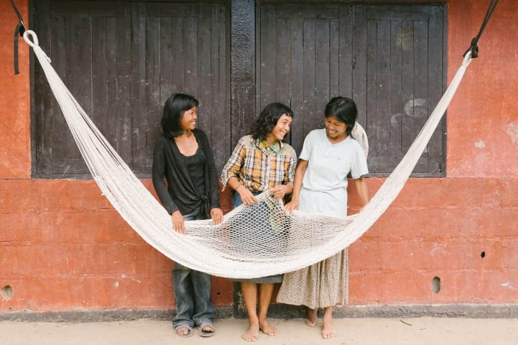 Three women pose in front of a hammock.
