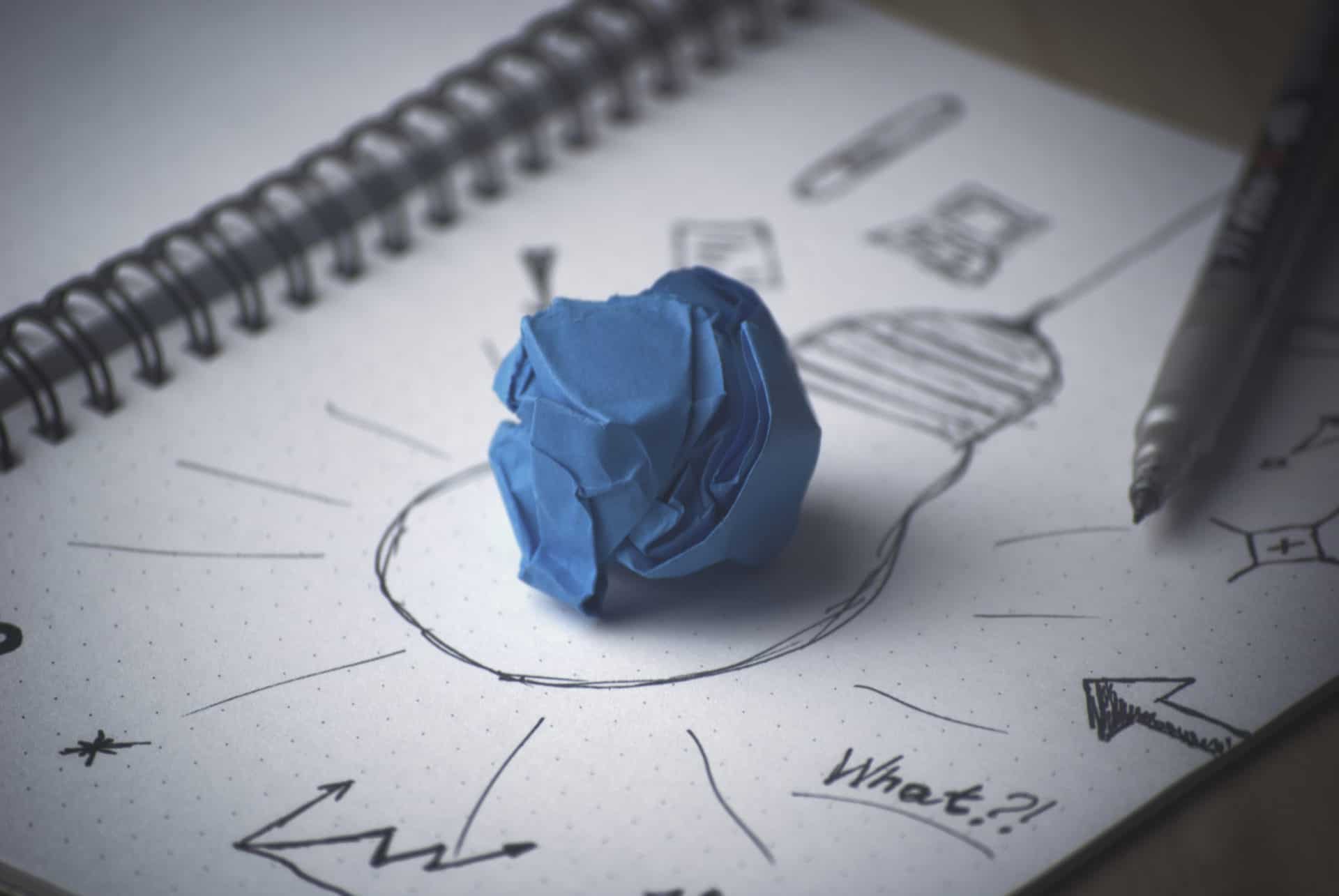 A crumpled sheet of blue paper sits on top of a pen and ink drawing of a lightbulb