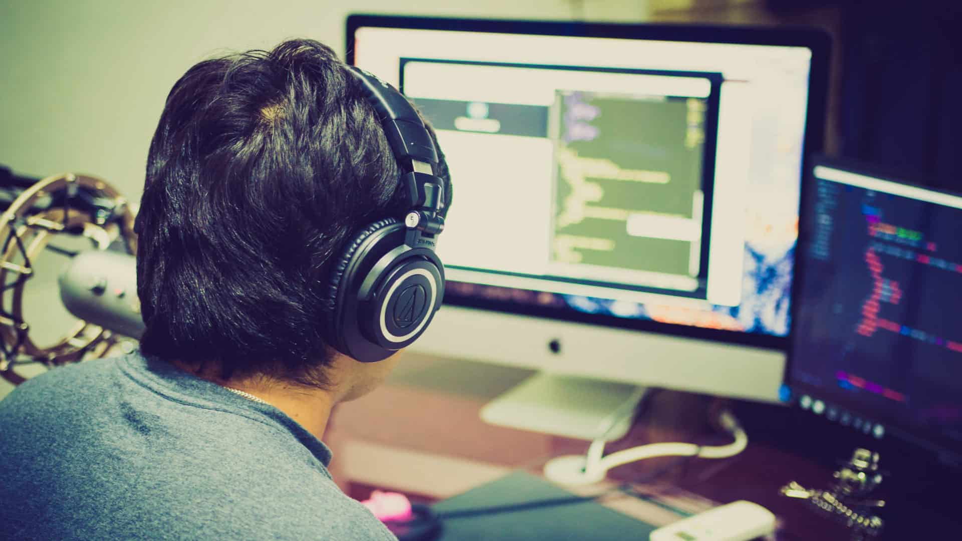 A man wearing headphones works at a computer station.