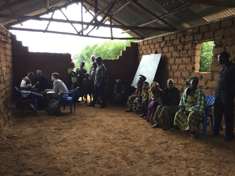 A group of people waiting along a wall during group prototyping in an African village