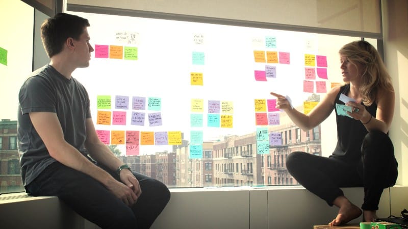 A woman and man talking about design strategy and looking at post it notes