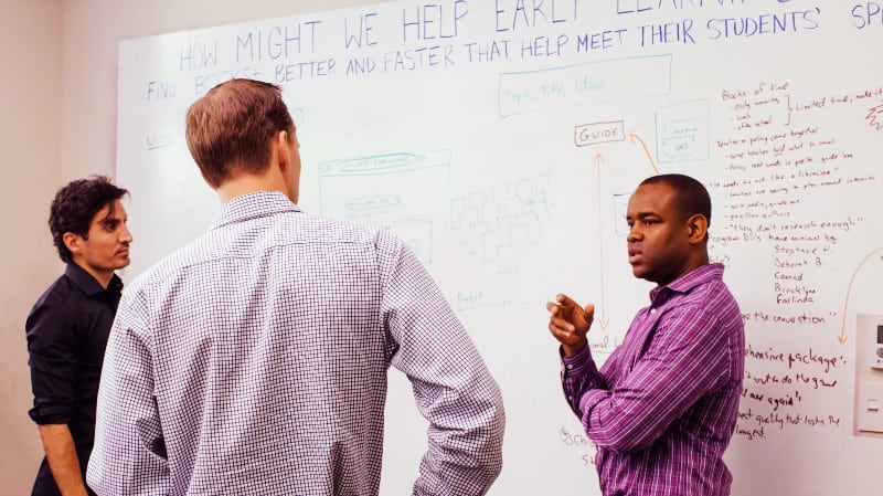 An HCD workshop for an education website where a group of men talking in front of a whiteboard covered in notes