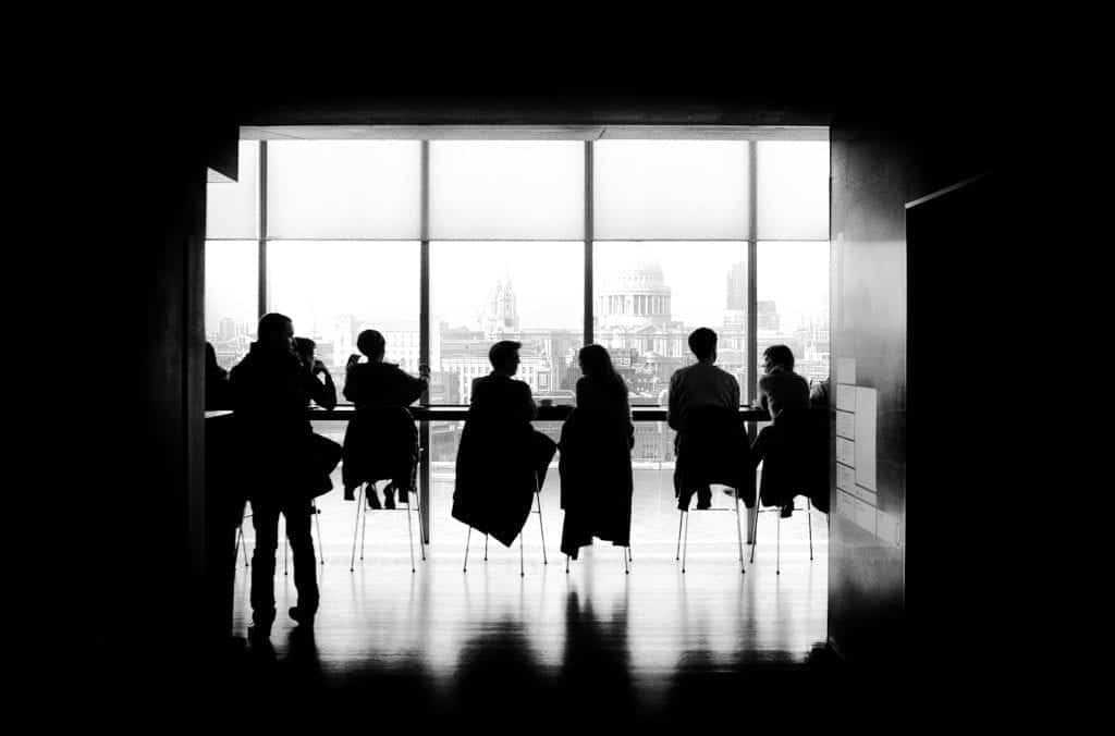 Black and white photo of people sitting facing large windows that look out onto a city skyline
