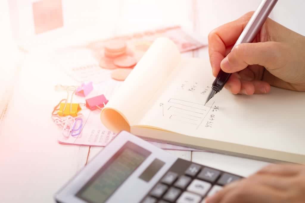 Close up of an accountants hands working at a calculator and yellow tablet.