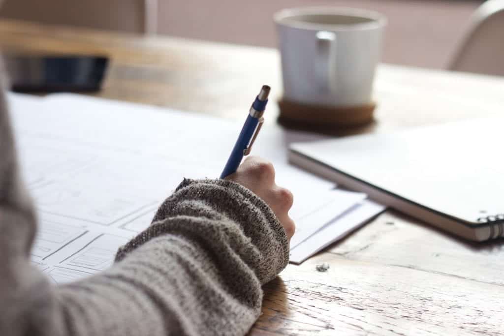 A designer works at a rustic table sketching wireframes.