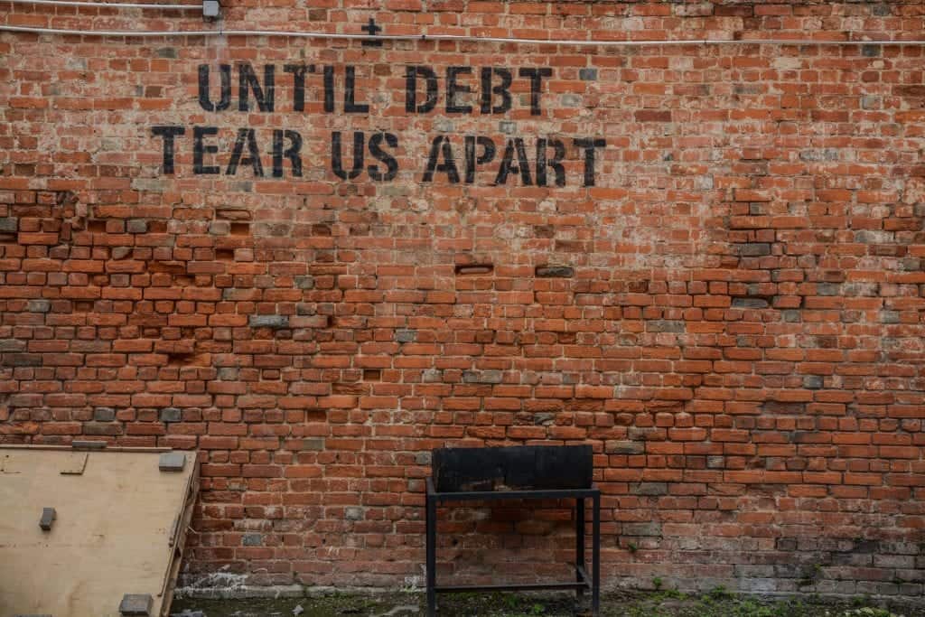 Until Debt Tear Us Apart painted on a brick wall.