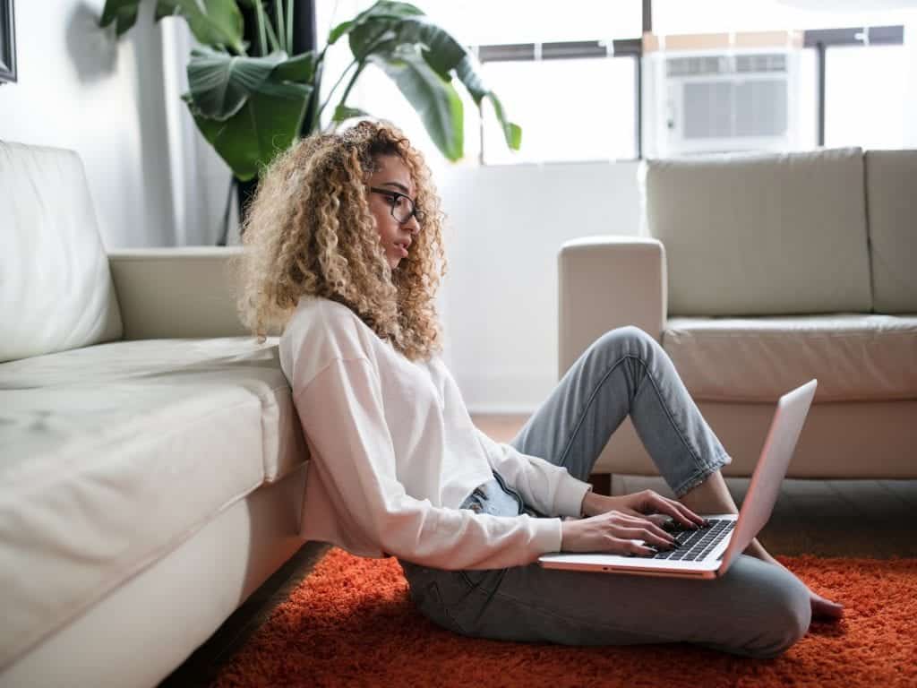 A young woman sits on the floor while using her laptop.