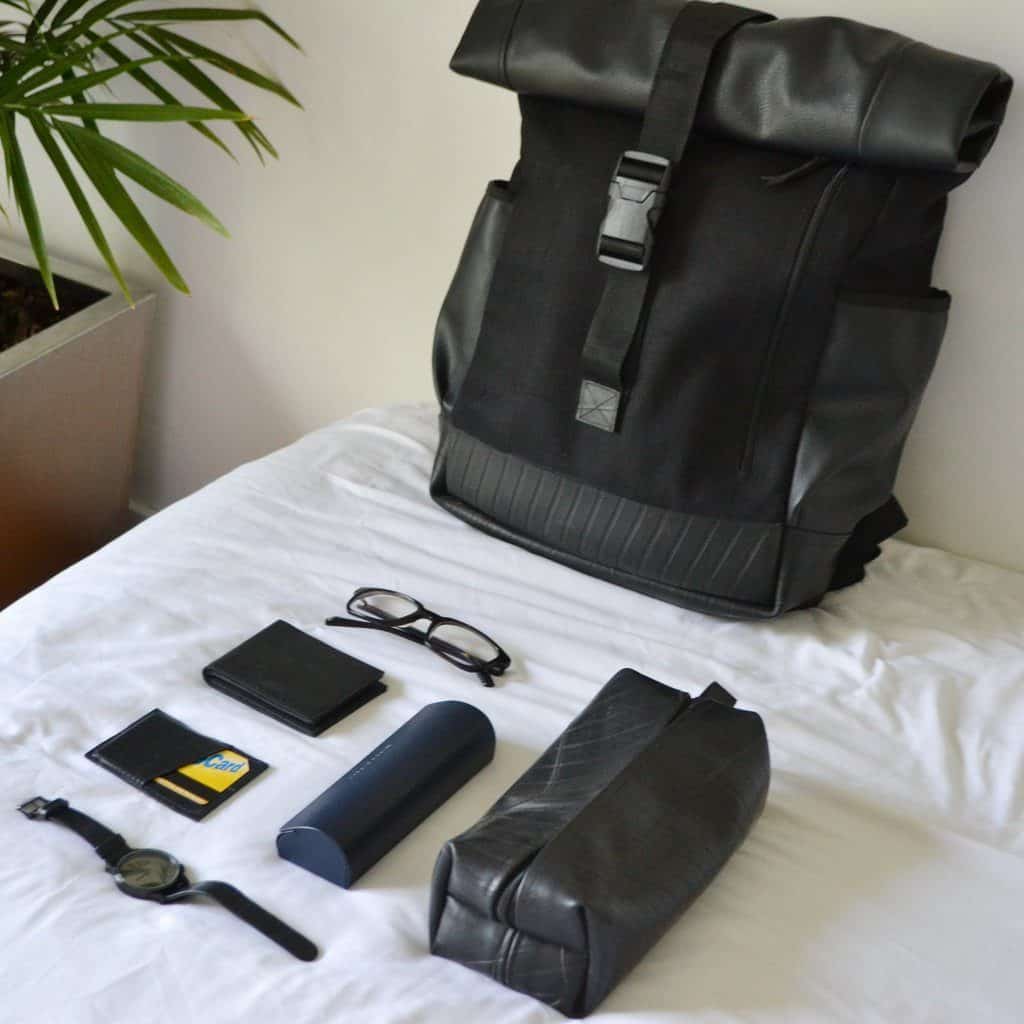 A black backpack on a bed with black accessories.