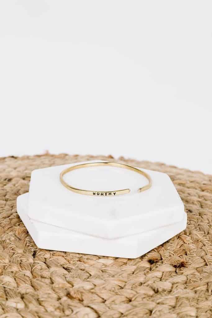 A gold bracelet that says worthy on marble coasters