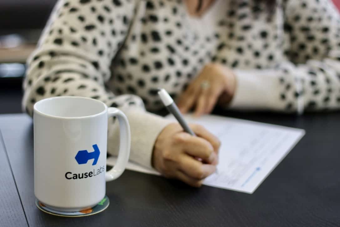 A person's hands writing and a CauseLabs coffee mug