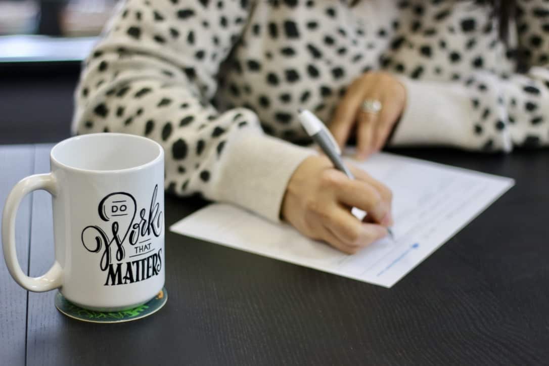 A person's hands writing and a Do Work That Matters coffee mug