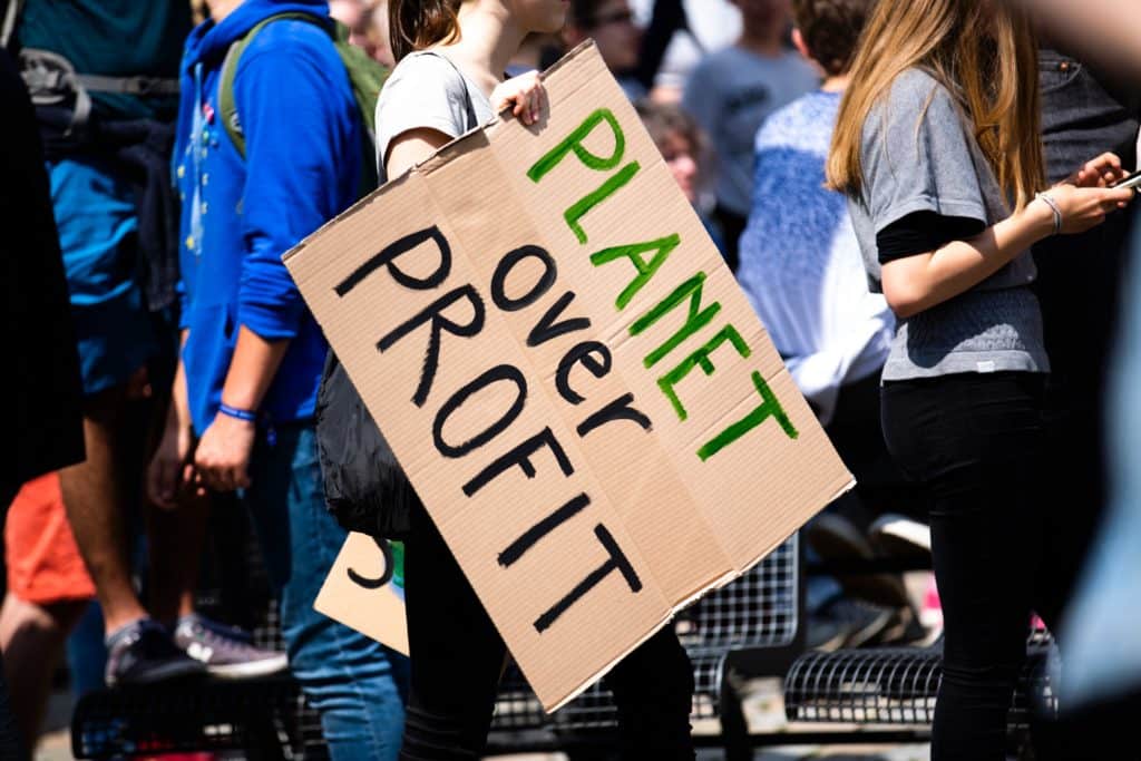 A woman in a crowd holding a sign that says planet over profit.