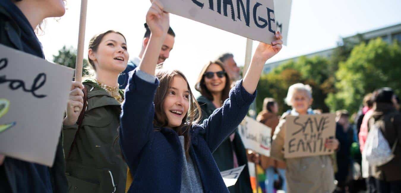 A young girl stands in a crowd holding a sign that says "change"