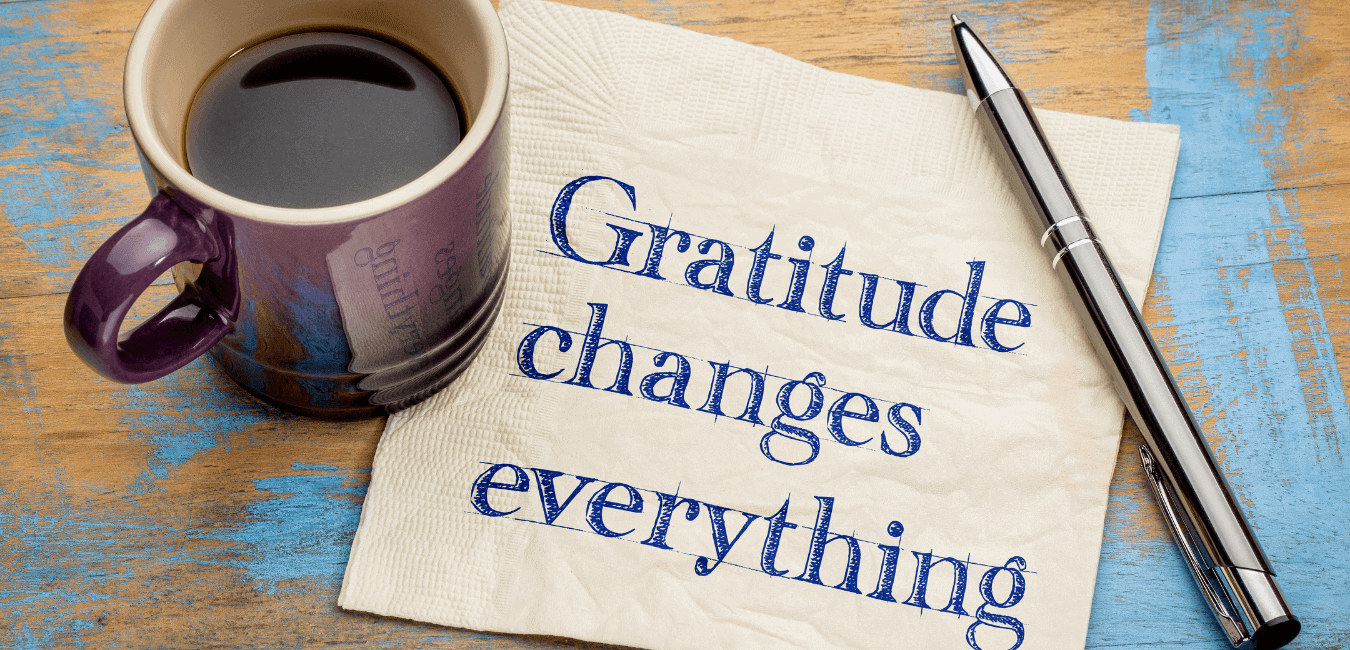 A coffee cup and pen on top of a paper with the words printed: Gratitude Changes Everything