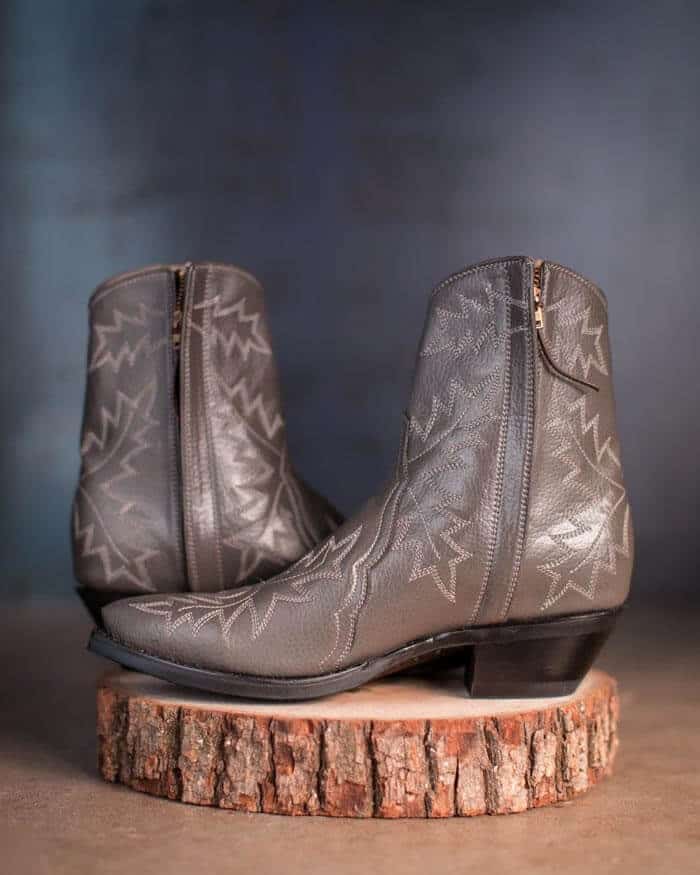 Pair of leather brown boots with leave prints on top of wood