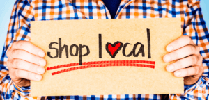 Man wearing checkered long sleeve holding a shop local sign