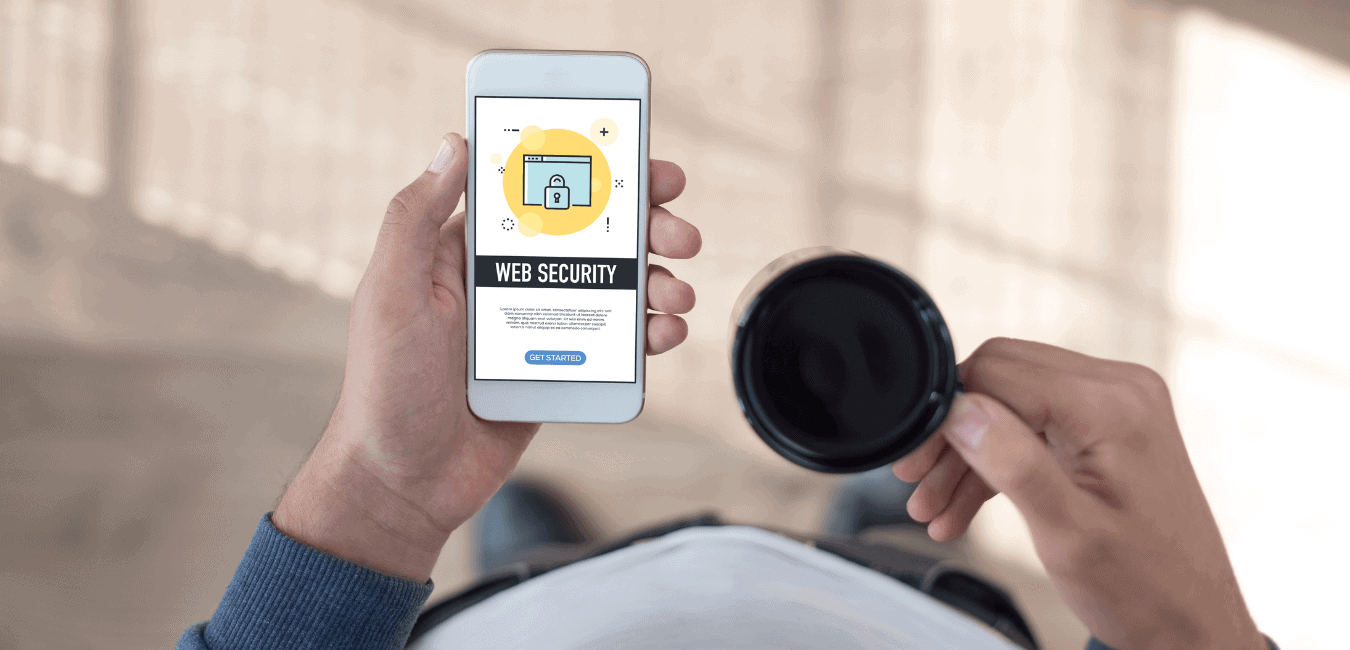 Man wearing blue sweater holding a cup of coffee and Web Security prompt on a cellphone with the other hand