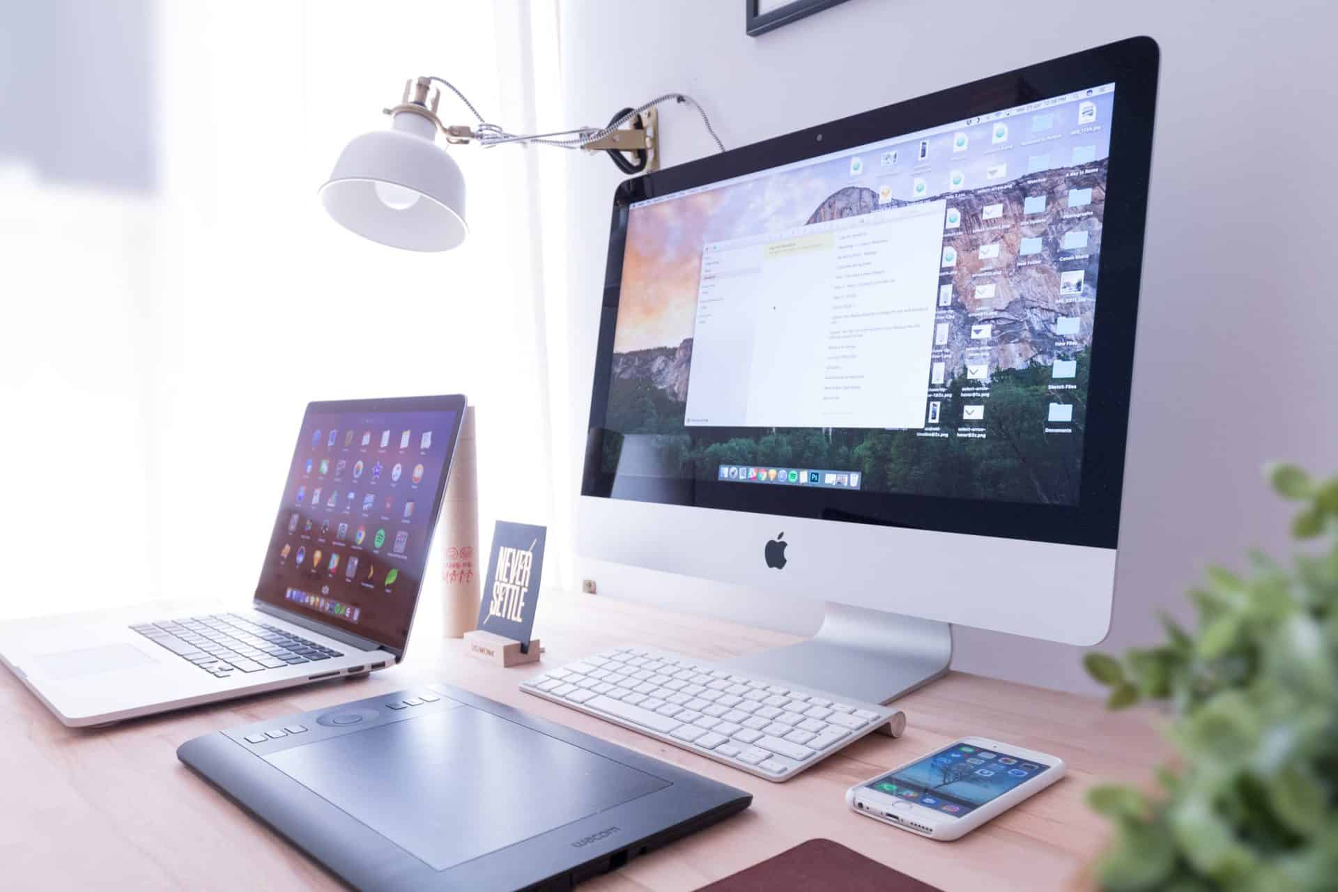 Different devices on a desk including an iMac, a laptop, a tablet, and a phone.