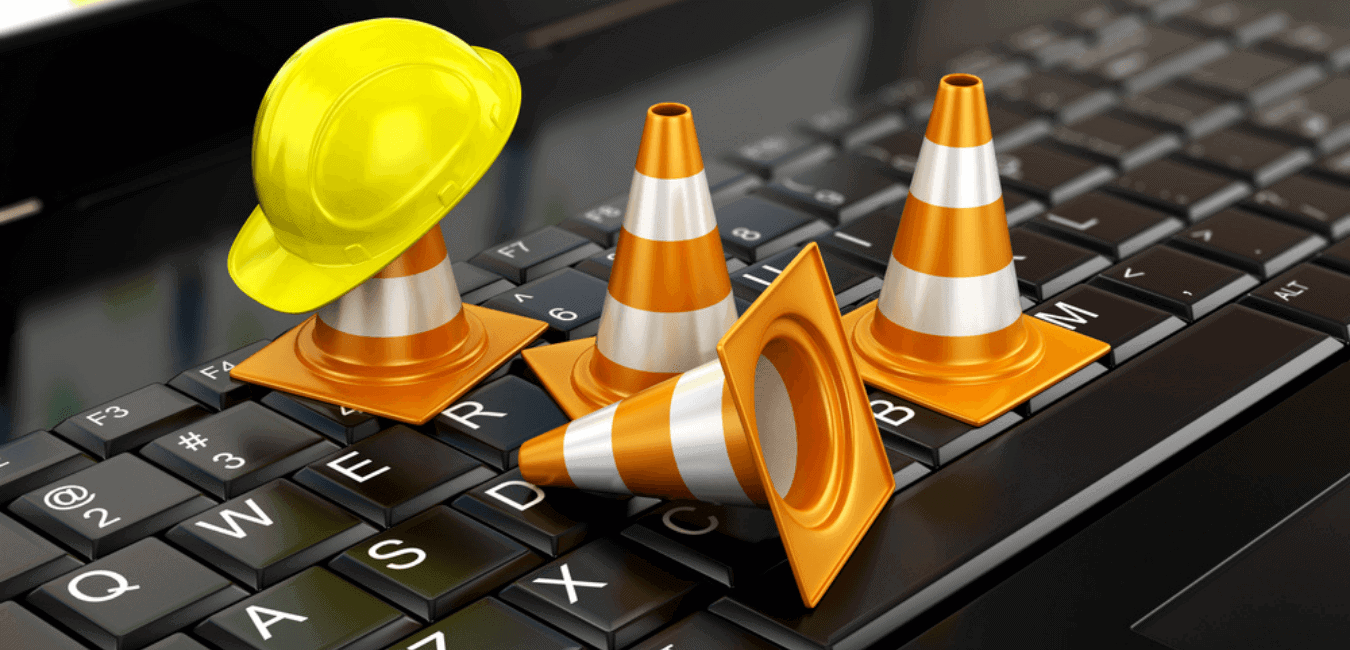 Construction cone and hat on top of laptop keyboard for website maintenance