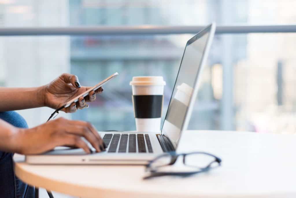 A woman's hands typing on a laptop and a smartphone