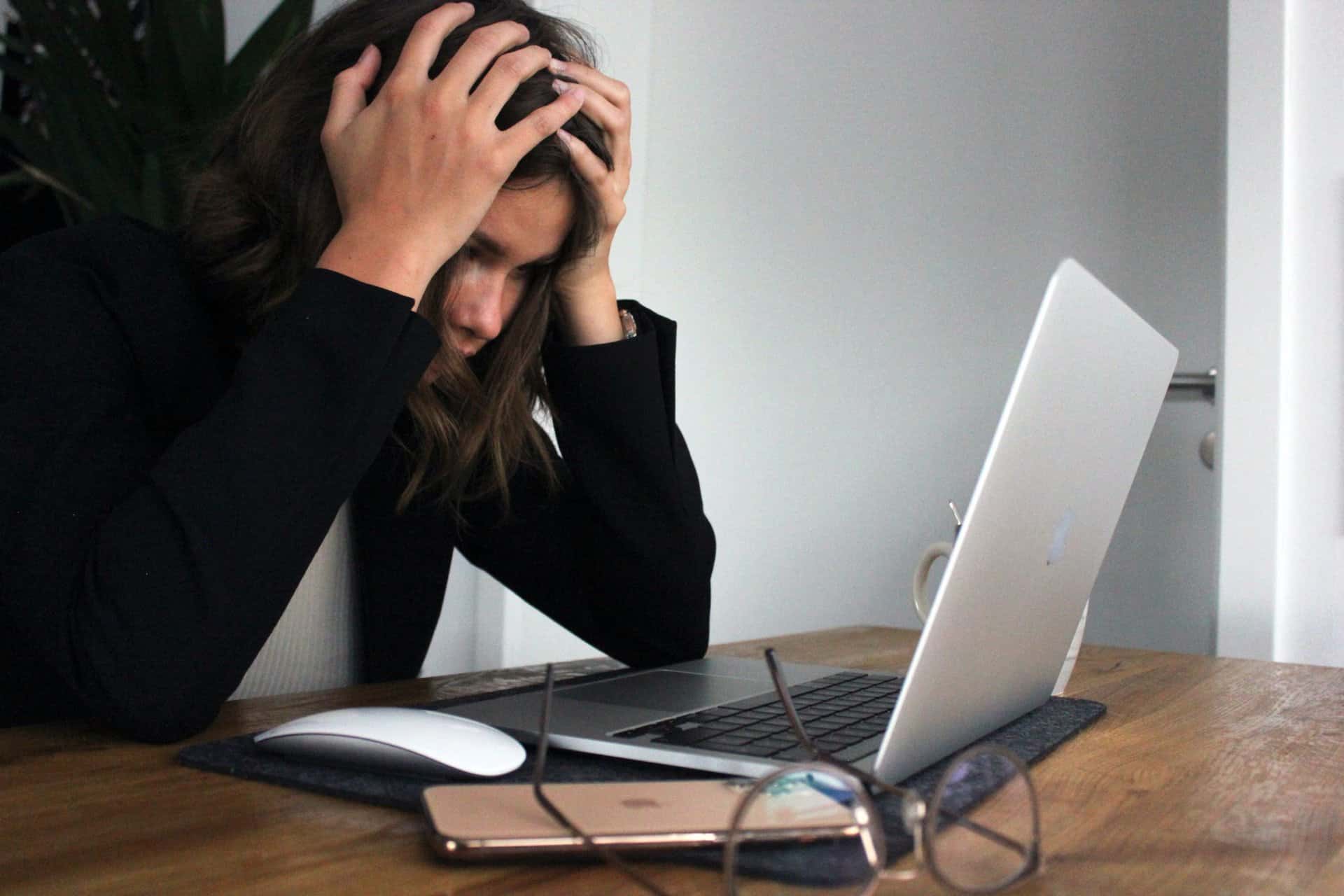 Woman looking at a laptop screen with her hands on her head in frustration