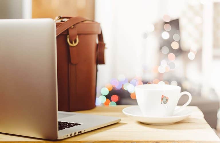 A laptop, tea cup, and work bag on a table.