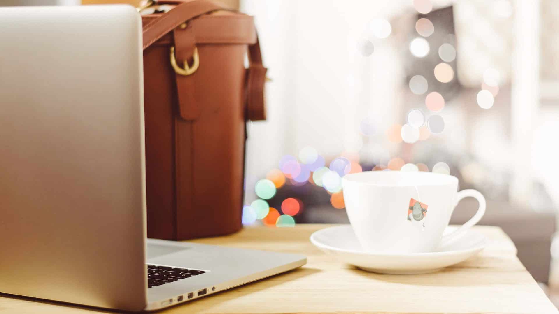 A laptop, tea cup, and work bag on a table.