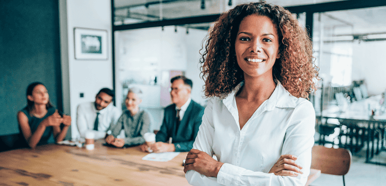 Woman of color with natural hair smiling in front of her team in office. An image for our risk management and risk mitigation post.
