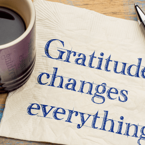 A coffee cup and pen on top of a paper with the words printed: Gratitude Changes Everything