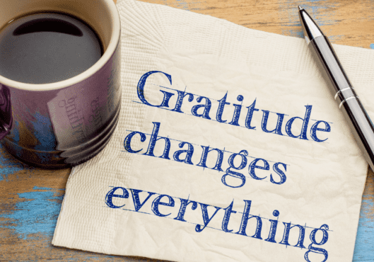 A coffee cup and pen on top of a paper with the words printed: Gratitude Changes Everything