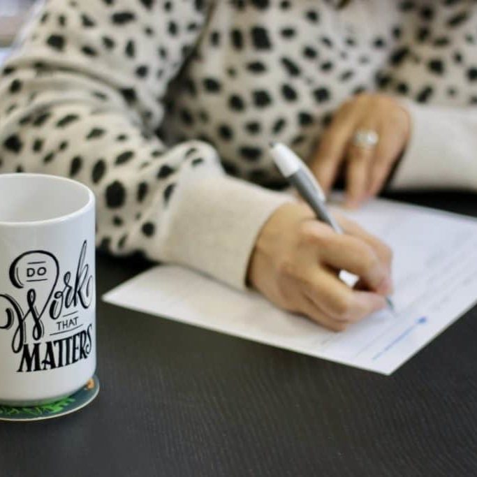 A person's hands writing and a Do Work That Matters coffee mug