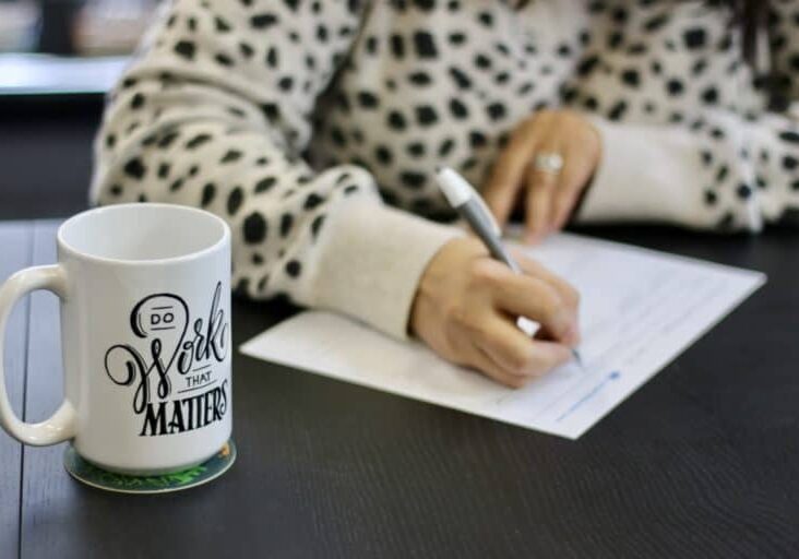 A person's hands writing and a Do Work That Matters coffee mug