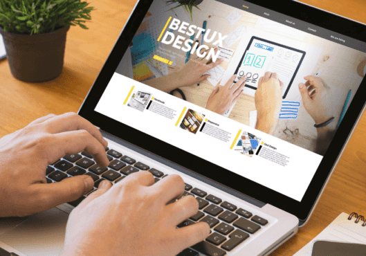 Man using his laptop creating and navigating website besides his glasses and phone