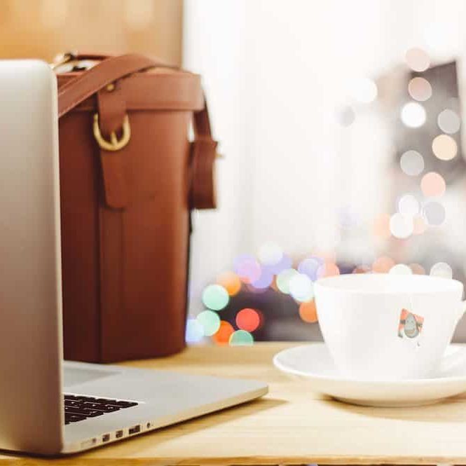 A laptop, tea cup, and work bag on a table.