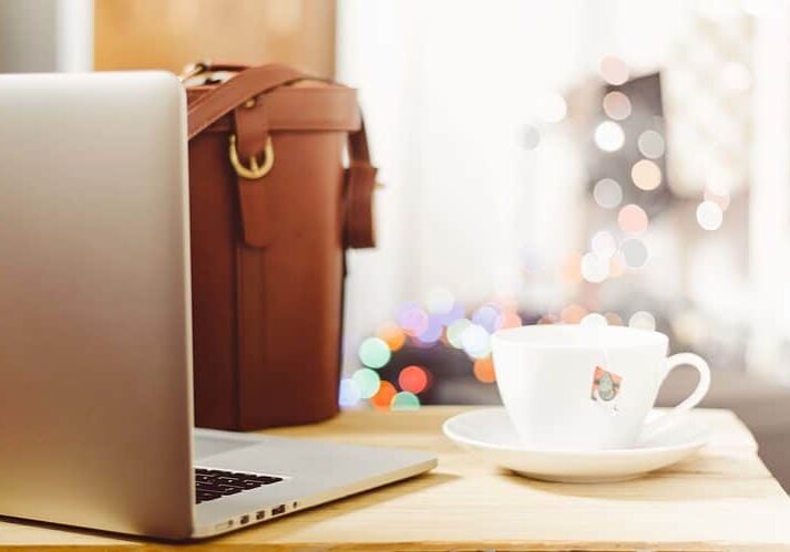 A laptop, tea cup, and work bag on a table.