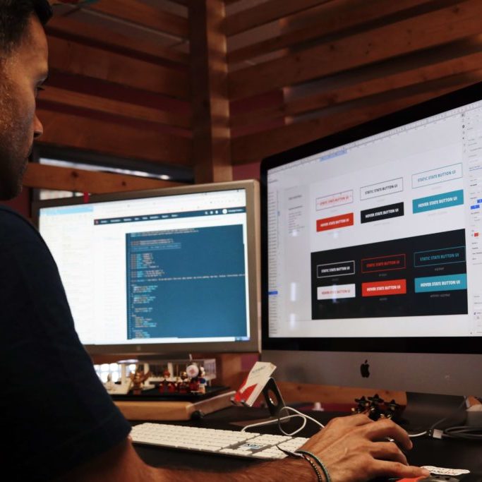 A man designing a website on two computer monitors.