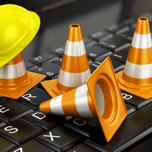 Construction cone and hat on top of laptop keyboard for website maintenance