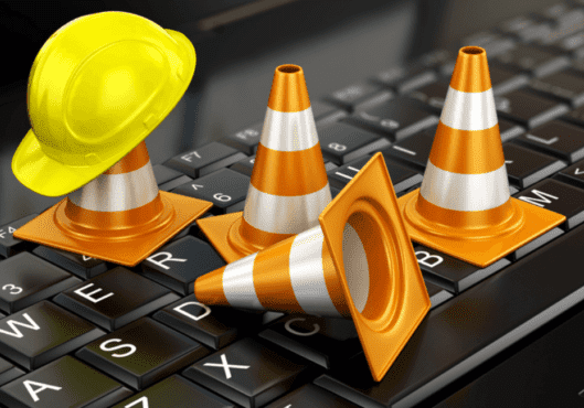 Construction cone and hat on top of laptop keyboard for website maintenance