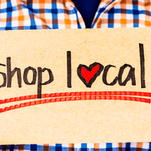 Man wearing checkered long sleeve holding a shop local sign