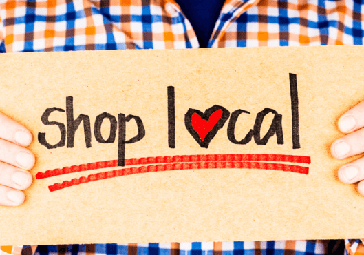 Man wearing checkered long sleeve holding a shop local sign