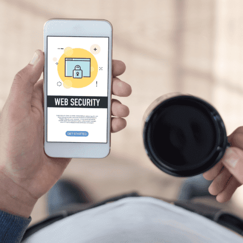 Man wearing blue sweater holding a cup of coffee and Web Security prompt on a cellphone with the other hand